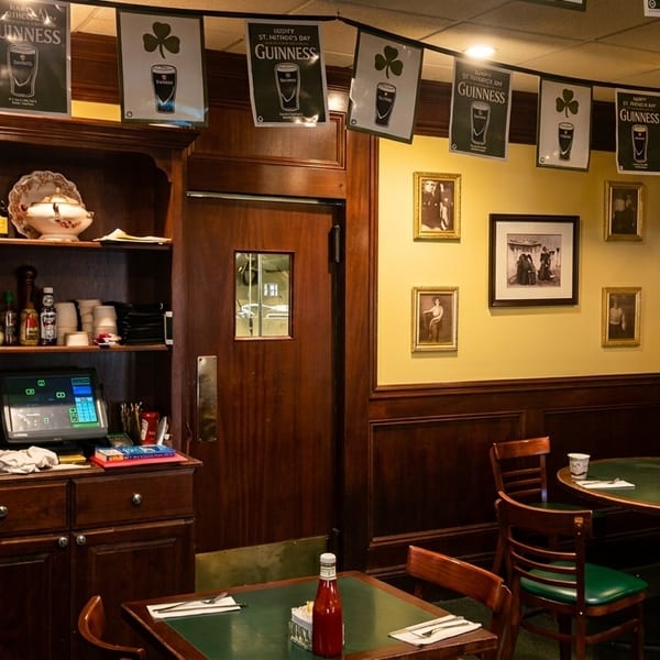 Cozy Irish pub interior with Guinness banners, dark wood, yellow walls, and green-topped tables.