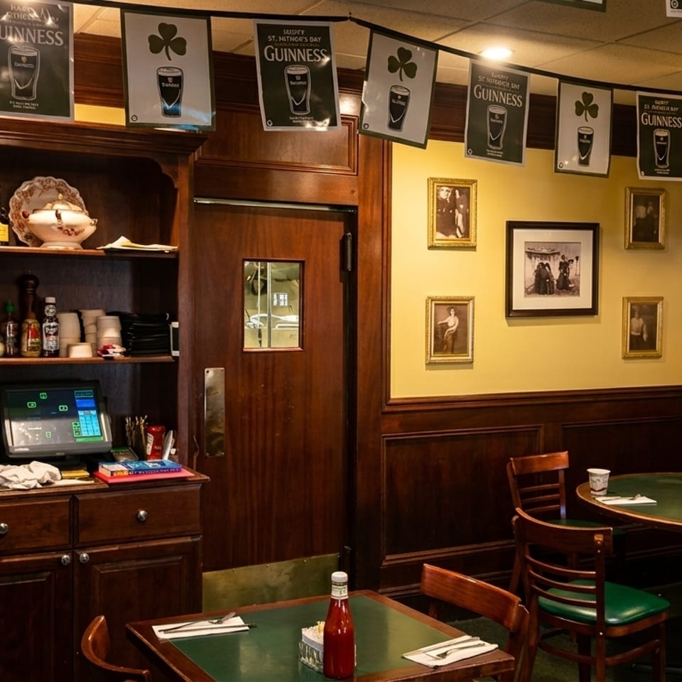 Cozy Irish pub interior with Guinness banners, dark wood, yellow walls, and green-topped tables.